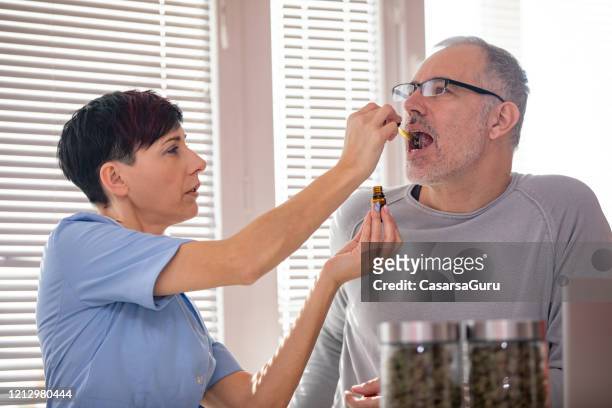 trabajador de la salud alternativa dejando caer el aceite de cbd en la lengua del paciente - cannabis oil fotografías e imágenes de stock