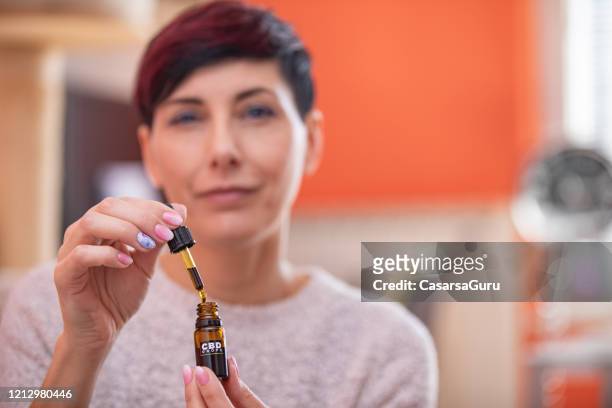 portrait of content adult woman holding cbd oil drops in domestic room - cbd oil stock pictures, royalty-free photos & images