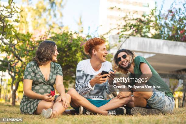 menschen, die auf dem rasen sitzen und musik auf dem mp3-player hören - 3 teenagers mobile outdoors stock-fotos und bilder