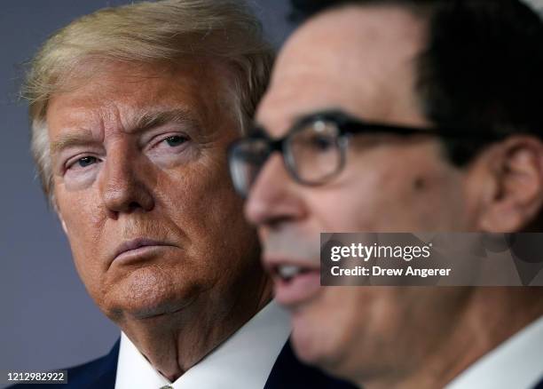 President Donald Trump listens to Secretary of the Treasury Steven Mnuchin speak during a briefing about the coronavirus in the press briefing room...