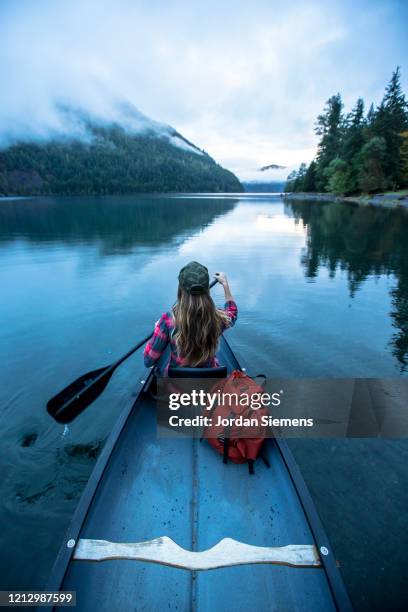 a woman paddling a canoe across a calm lake with fog in the distance - boat top view stockfoto's en -beelden