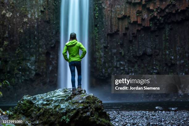 a woman in a green raincoat standing in front of a waterfall. - behind waterfall stock-fotos und bilder