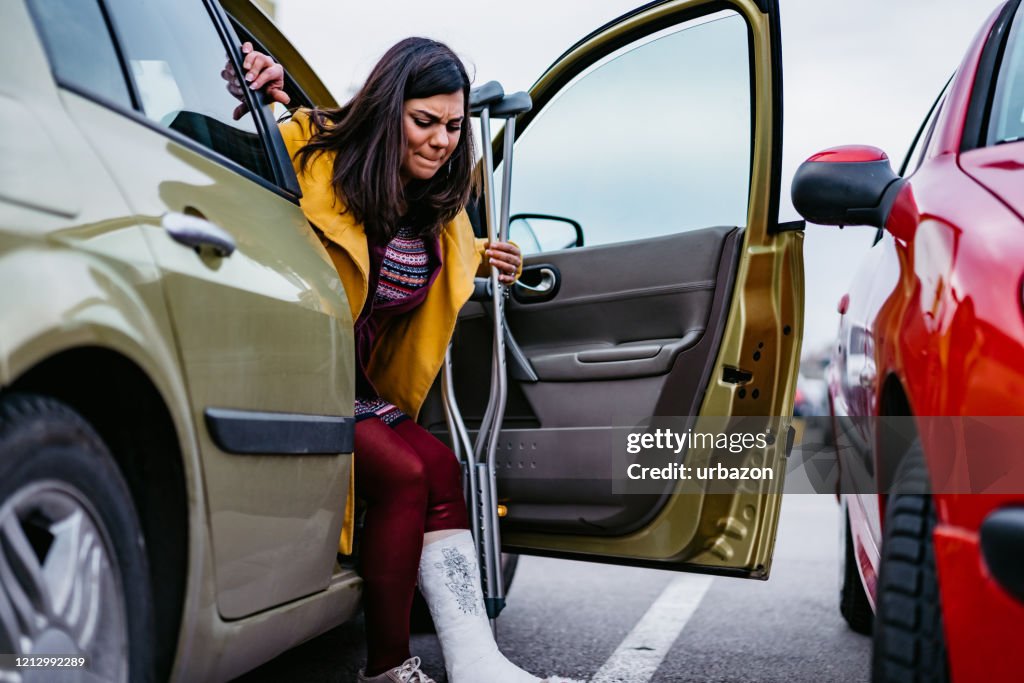 Frau mit Cast steigt aus Auto
