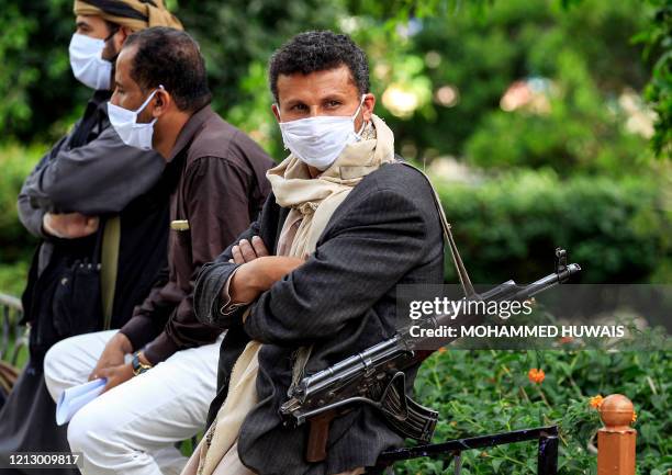 Fighter loyal to Yemen's Huthi rebels acting as security, looks on while wearing a face mask and latex gloves and slinging a Kalashnikov assault...