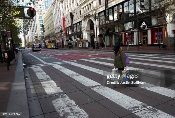 Pedestrian carries two packages of toilet paper as she crosses an empty Market Street on March 17, 2020 in San Francisco, California. Seven San...