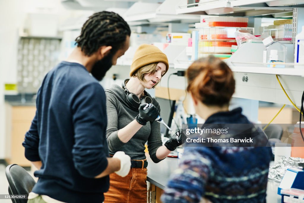 Scientists in discussion while pipetting samples in research lab