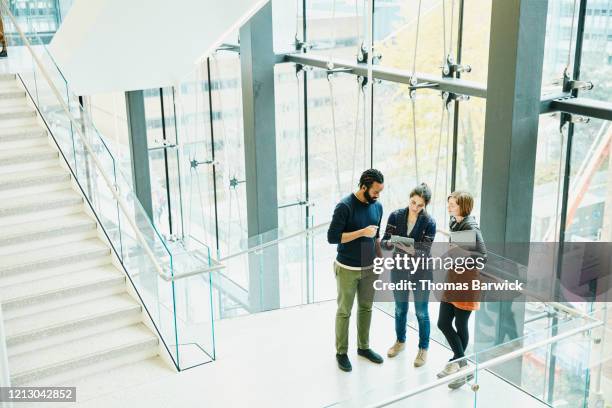 coworkers discussing project on digital tablet on stairs of office building - businessperson stairs photos et images de collection