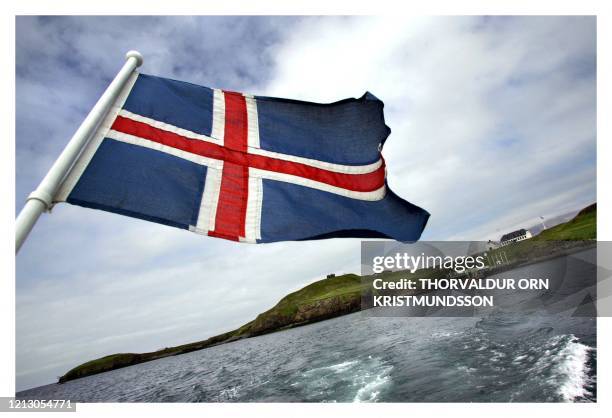 Iceland flag flaps on October 13, 2008 as a boat leaves the Videy Island. Videy is the largest island of the Kollafjord Bay with its highest point...