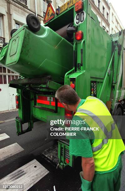 Un employé de la ville de Paris vide des poubelles destinées aux ordures ménagères dans la benne du camion, en août 2002 à Paris.