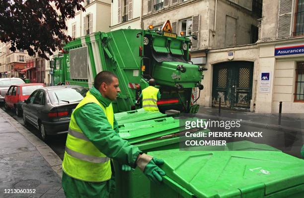 Un employé de la ville de Paris vide des poubelles destinées aux ordures ménagères dans la benne du camion, tandis que l'un de ses collègues remet...