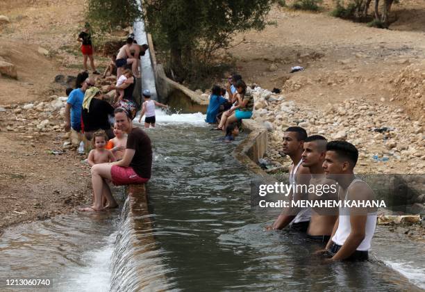Palestinian youths and Jewish settlers gather at a water spot near the occupied West Bank village of al-Auja in the Jordan valley on May 15 as the...
