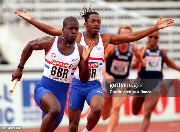 Der britische Sprinter Marlon Devonish breitet die Arme aus. Sein Teamgefährte Dwain Chambers hat von ihm den Staffelstab übernommen und läuft los....