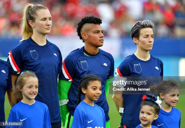 Sam Mewis of the United States, Adrianna Franch, and captain Megan Rapinoe stand on the field during player introductions with their tops turned...