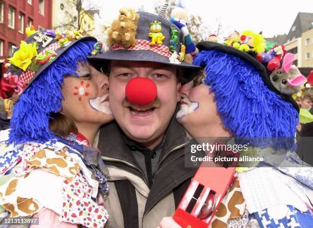 Zwei verkleidete junge Damen küssen am auf dem Alter Markt in Köln einen Herren mit roter Clownsnase auf seine Wangen. Die "fünfte Jahreszeit" hat...