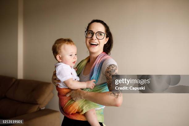 mujer joven sosteniendo a su bebé y sonriendo - portabebés fotografías e imágenes de stock