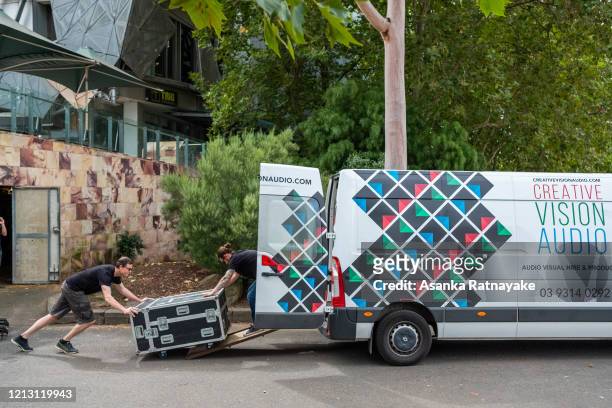Audio visual technicians push audio visual equipment out of Federation Square into a van on March 18, 2020 in Melbourne, Australia. The Prime...