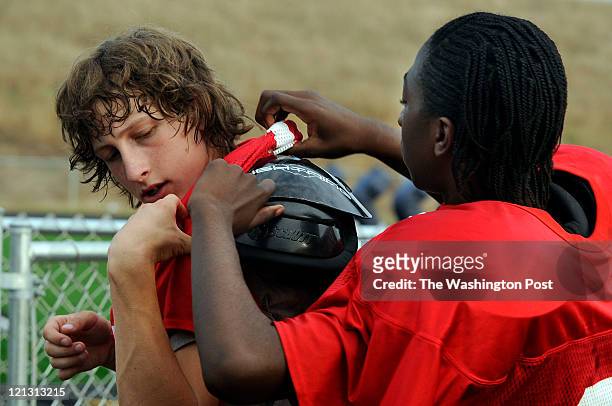 Players trying out for the Patriot Football Team put on shoulder pads before morning practice on August 9, 2011. Marshall Well gets help from Robert...