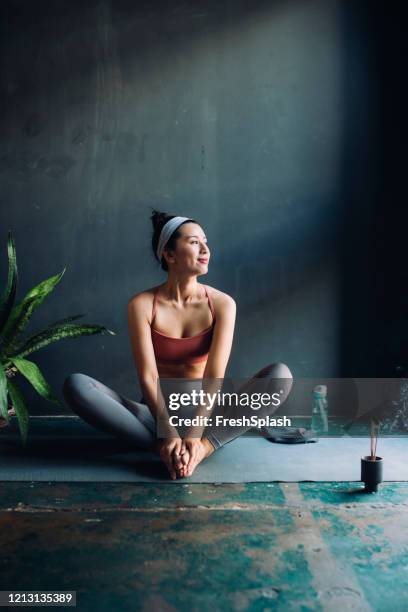 mujer asiática sentada en una alfombra de ejercicio y calentando para una sesión de yoga - asian sunshine fotografías e imágenes de stock