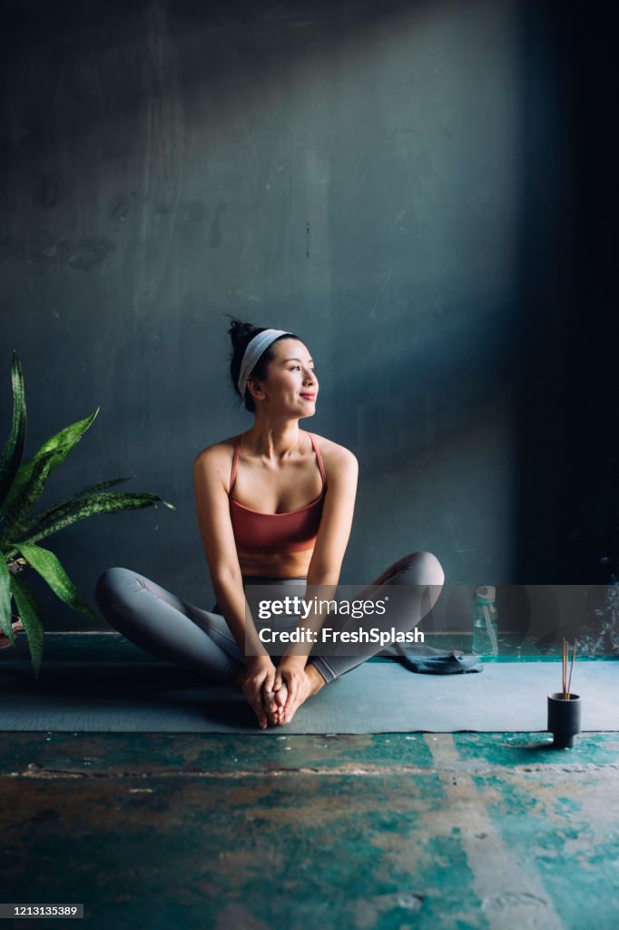 Asian Woman Sitting on an Exercise Mat and Warming Up for a Yoga Session