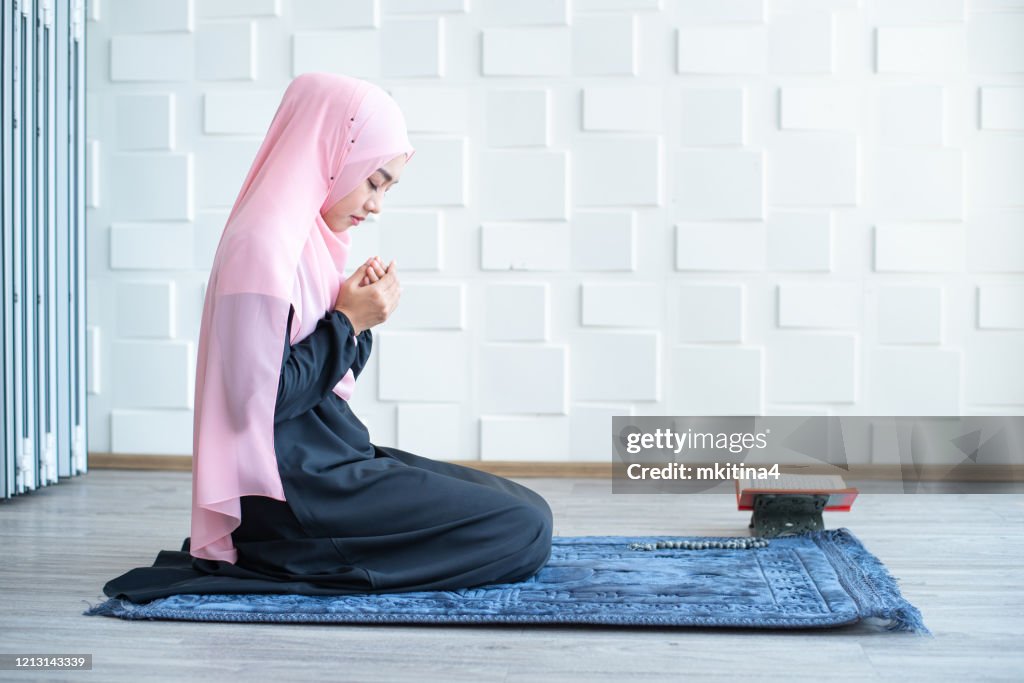 Side view of asian beautiful young muslim student woman prayer in hijab praying on carpet mat indoors