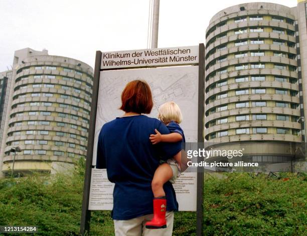 Eine Frau mit einem Kind im Arm betrachtet am 5.8.1999 den Übersichtsplan vor der Universitätsklinik Münster. Seit dem 26. Juli wird hier Raissa...