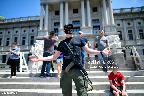 Man with an assault rifle reacts while joining demonstrators outside the Pennsylvania Capitol Building to protest the continued closure of businesses...