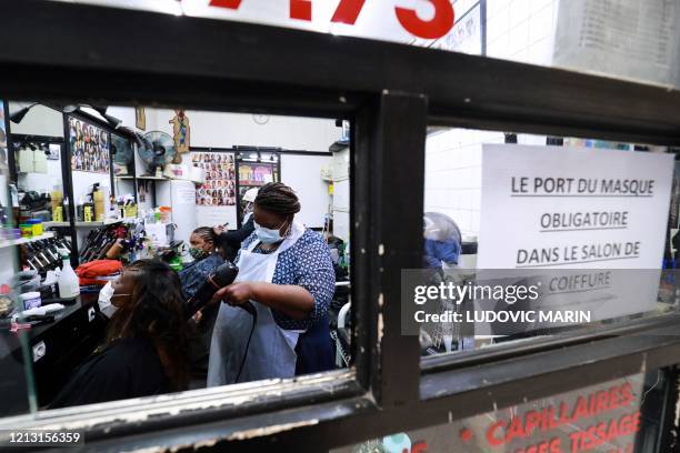 Hairdressers wearing protective facemasks style the hair of customers at an Afro hairdresser salon in Paris, on May 15, 2020 as France eases lockdown...