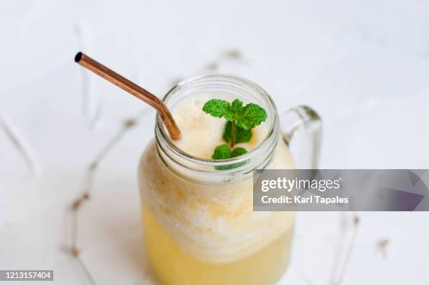 pineapple smoothie in a mason jar with metal straw on a white wooden table - yellow smoothie stock pictures, royalty-free photos & images