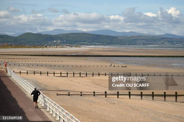People take their daily excercise on the promenade alongside a deserted beach in Rhyl, north Wales on May 16 following an easing of lockdown rules in...
