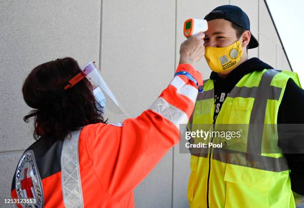 Member of the Red Cross measures the temperature of a security officer at the entrance of the stadium prior to the Bundesliga match between TSG 1899...