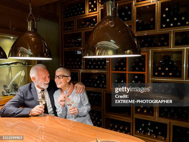 senior couple having romantic time together in a wine room while tasting sparkling wine - wine rack stock pictures, royalty-free photos & images