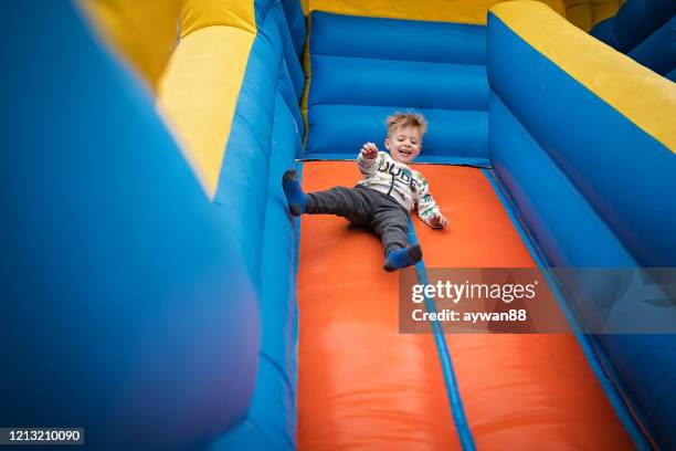 cute boy sliding down on a bouncy castle - inflatable playground stock pictures, royalty-free photos & images