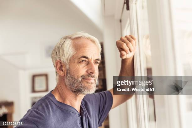 portrait of mature man looking out of window - homem 55 anos imagens e fotografias de stock