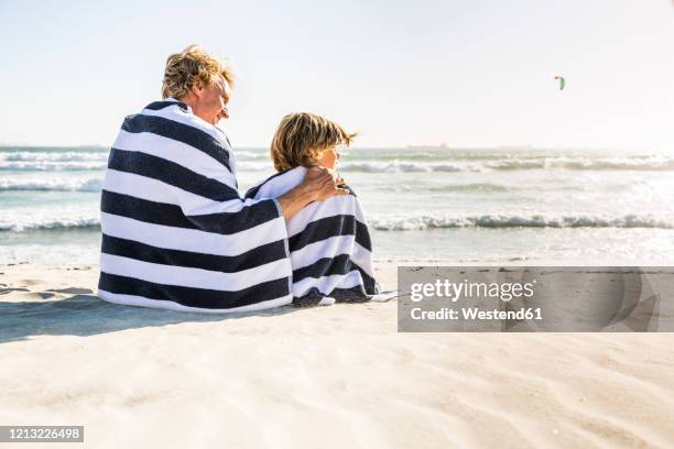 father with son wrapped in a towel on the beach - striped towel stock pictures, royalty-free photos & images