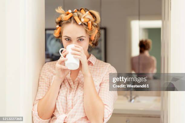 portrait of young woman with curlers in hair drinking coffee - hair curlers stockfoto's en -beelden