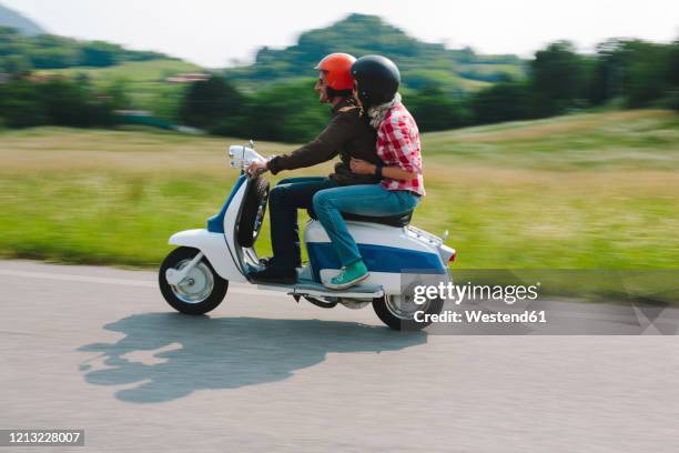 couple riding vintage motor scooter on country road, tuscany, italy - motorino foto e immagini stock