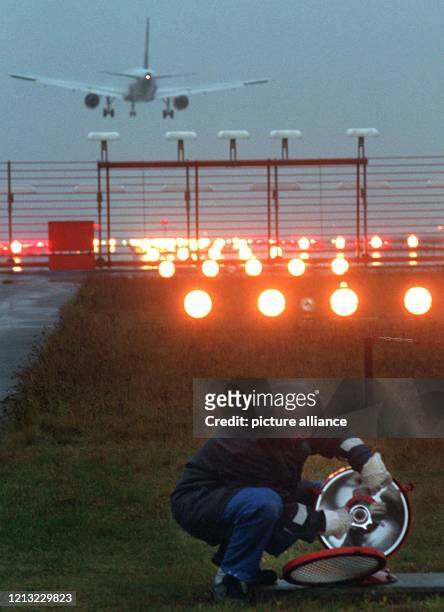 Ein Mitarbeiter des Frankfurter Flughafens kontrolliert im Morgengrauen eine Lampe an der Landebahn des Rhein-Main-Flughafens, im Hintergrund ein...