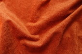 Soft folds on bright reddish orange artificial suede fabric