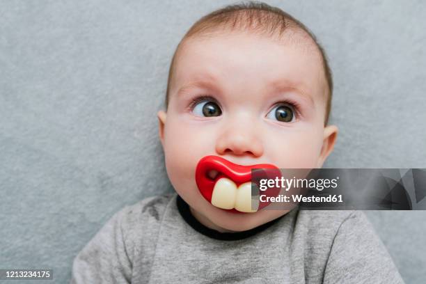portrait of baby girl with big teeth pacifier lying on grey blanket - big lips fotografías e imágenes de stock