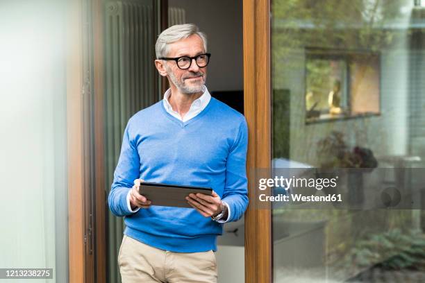 smiling senior man with grey hair standing in front of his modern design home holding tablet - reichtum stock-fotos und bilder