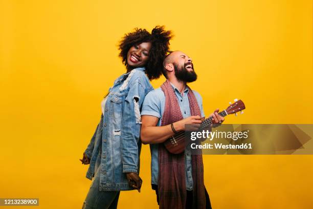 happy young man with woman in studio playing ukulele - couple coloured background stock pictures, royalty-free photos & images