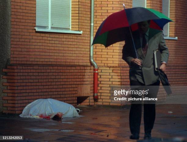 Ein Passant mit Regenschirm geht scheinbar achtlos an der zugedeckten Leiche eines, bei einer Schießerei in Herne ums Leben gekommenen Mannes,...