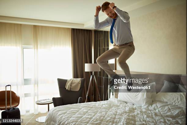 excited businessman jumping on bed in hotel room - jumping on bed stockfoto's en -beelden