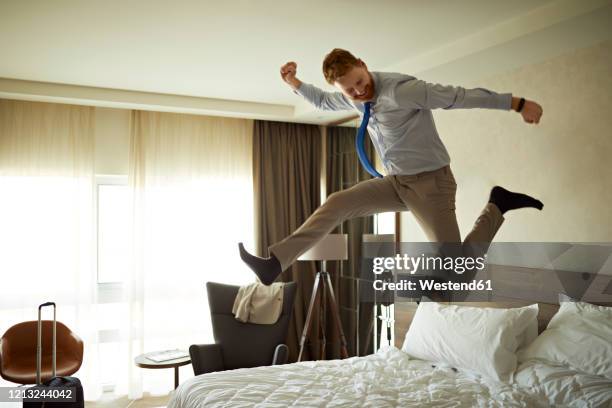 excited businessman jumping on bed in hotel room - jump on bed photos et images de collection