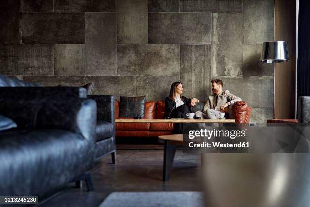 businessman and businesswoman sitting on couch in hotel lobby - business meeting coffee stock pictures, royalty-free photos & images