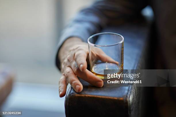 close-up of man with whiskey glass on arm rest of a leather chair - whiskey stock pictures, royalty-free photos & images