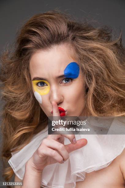 serious young woman with painted face in clown costume making silence gesture - hand opsteken stockfoto's en -beelden