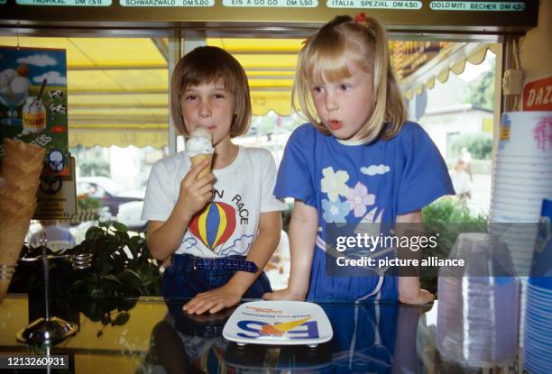 Zwei kleine Mädchen in einer Eisdiele, aufgenommen im August 1987. Während die eine schon glücklich an ihrer Eiswaffel leckt, überlegt die andere...