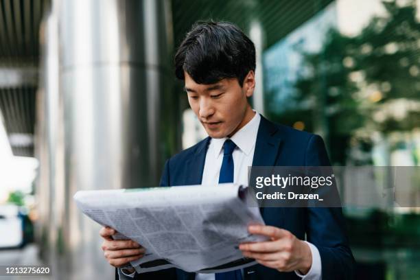 asian businessman in full suit reading printed newspaper near the office building - korean culture stock pictures, royalty-free photos & images