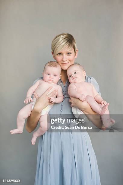 young mother holds up twins. - twins stock pictures, royalty-free photos & images